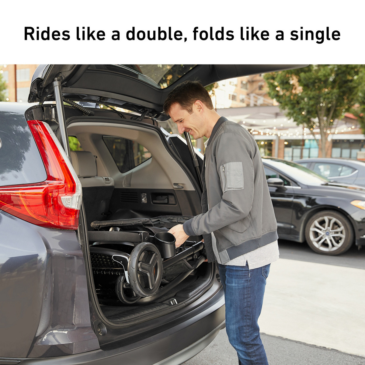A man loads the folded stroller, wheels and frame tucked flat, into the open trunk of an SUV on a street, with the burned-in headline 'Rides like a double, folds like a single'