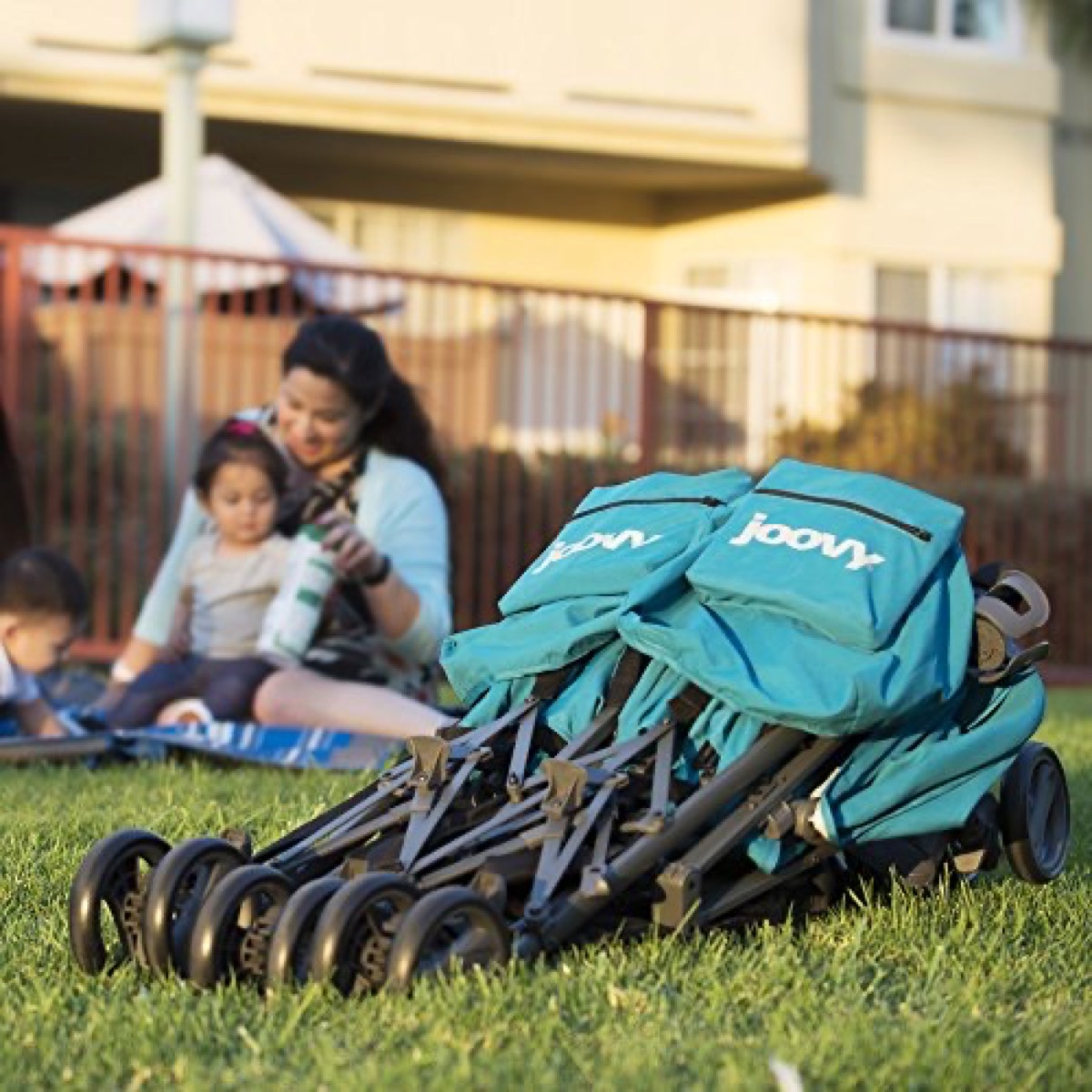 The Twin Groove Ultralight in Turquoise folded flat, standing on a lawn with a family seated at a blanket in the background
